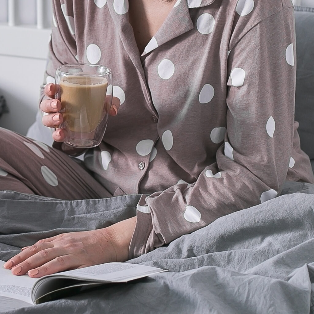 Woman sitting on bed holding cup with hot beverage in hands. Harmony, love youself wellbeing concept